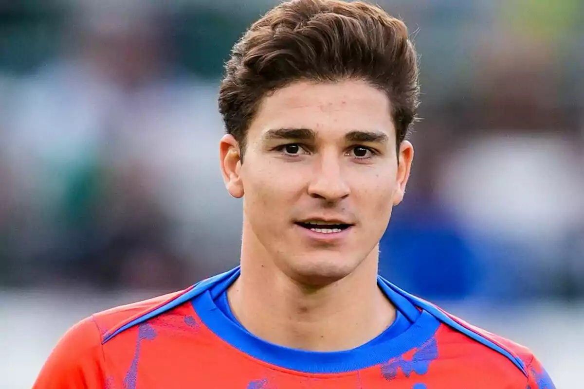 A young man with brown hair and a red sports jersey with blue details.