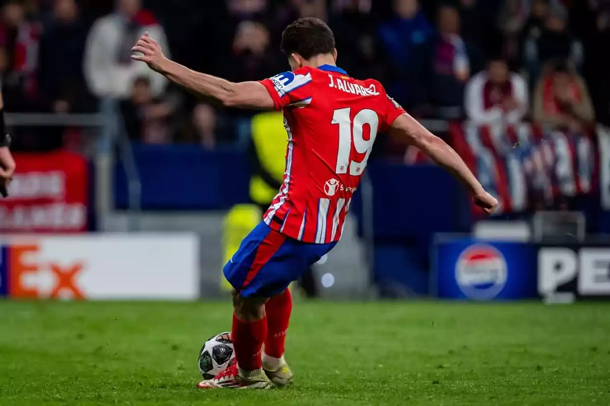 Jugador de fútbol con camiseta roja y azul número 19 pateando un balón en un estadio.