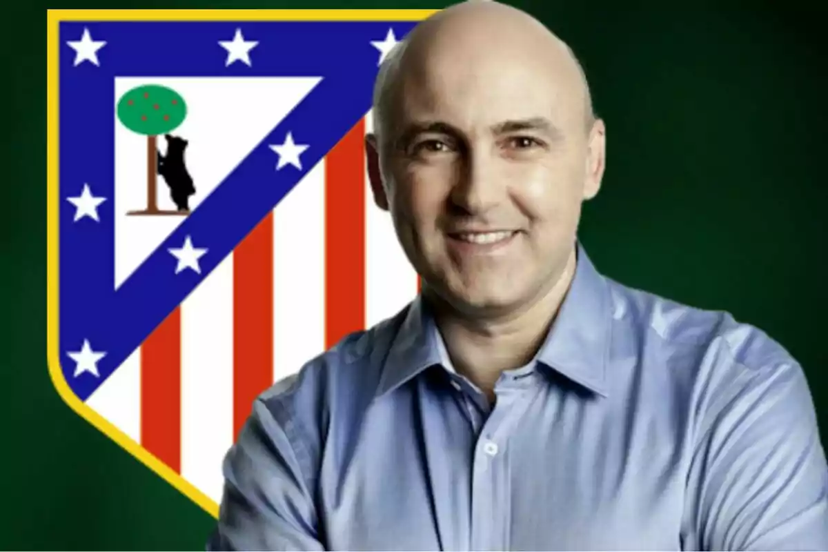 Un hombre sonriente con camisa azul está frente al escudo del Atlético de Madrid.