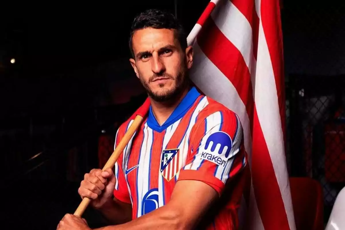 Un jugador de fútbol con la camiseta del Atlético de Madrid sostiene una bandera rojiblanca.