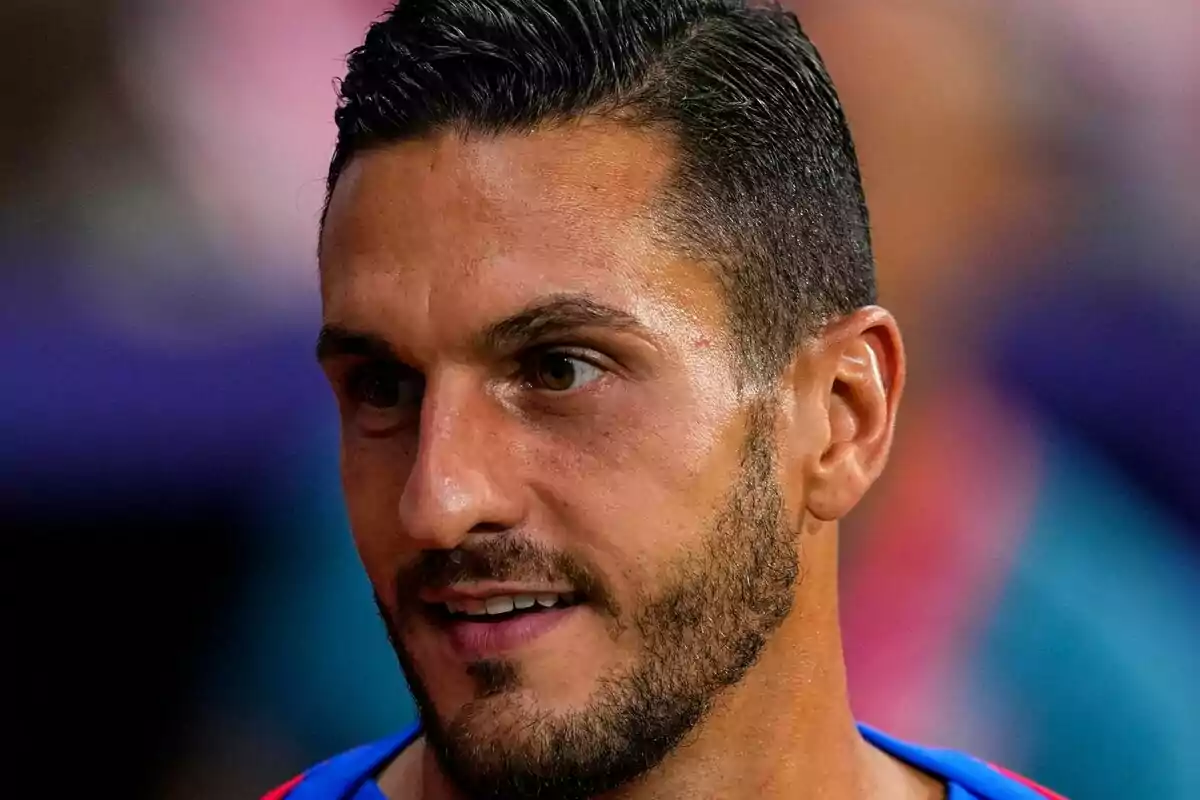 Un hombre con barba y cabello corto, vestido con una camiseta azul, mirando hacia la derecha.