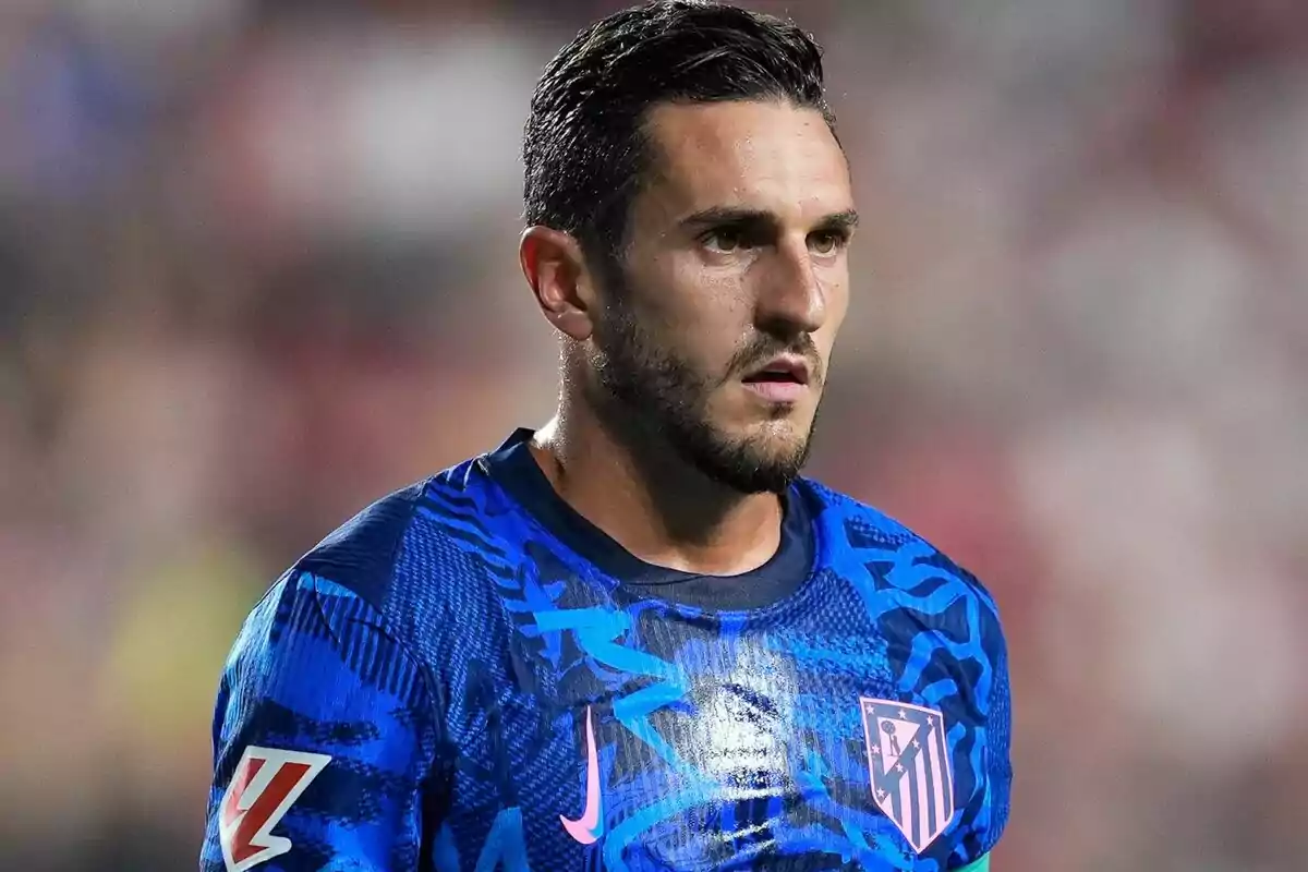 Jugador de fútbol con camiseta azul del Atlético de Madrid en un campo de juego.