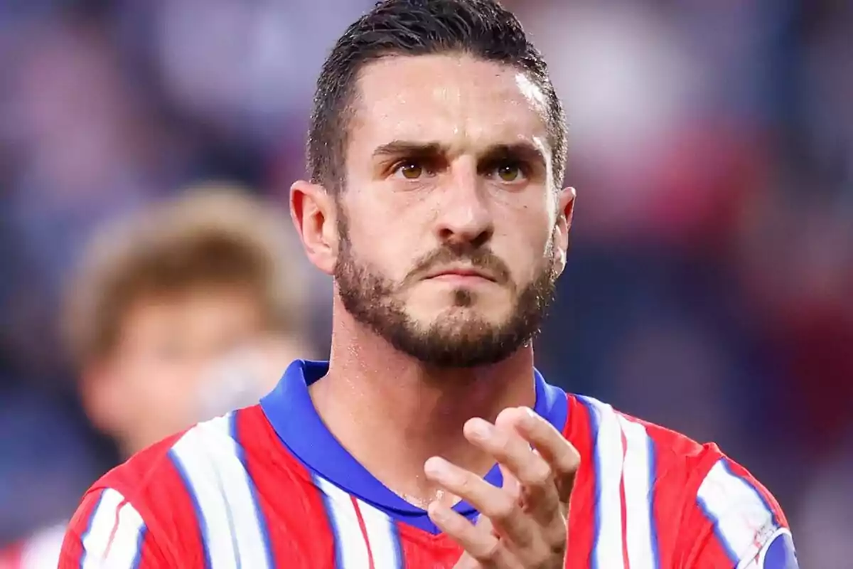 A player in a red and white striped jersey claps while looking forward with a serious expression.