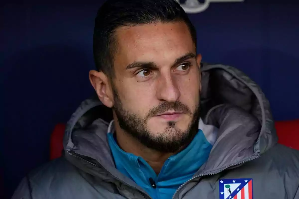 Un hombre con barba y cabello oscuro viste una chaqueta con el escudo del Atlético de Madrid.