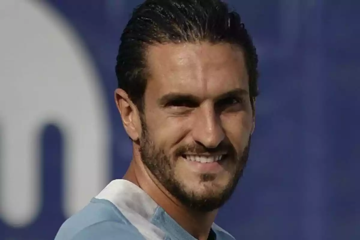 Hombre de cabello oscuro y barba corta sonriendo con camiseta celeste