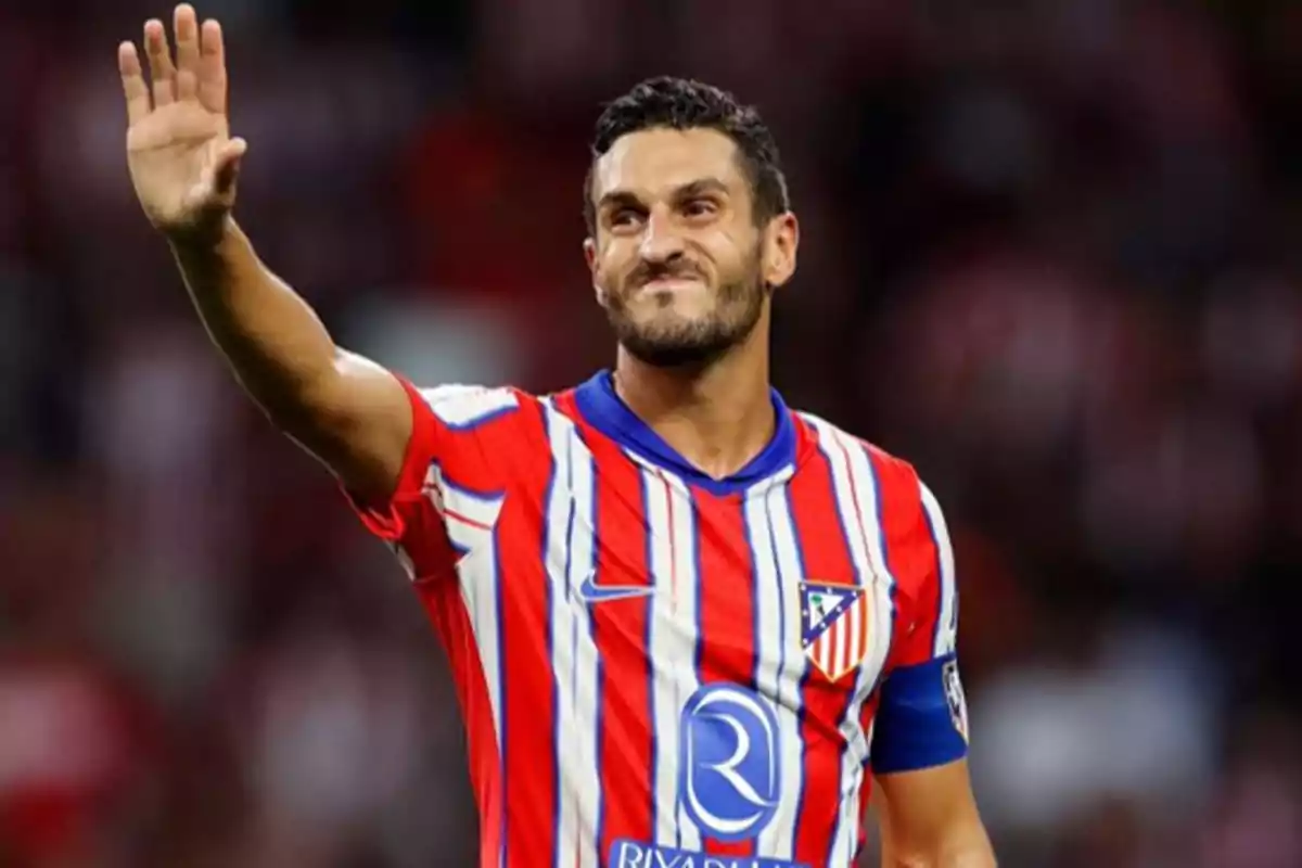 Jugador de fútbol con uniforme rojo y blanco levantando la mano en señal de saludo