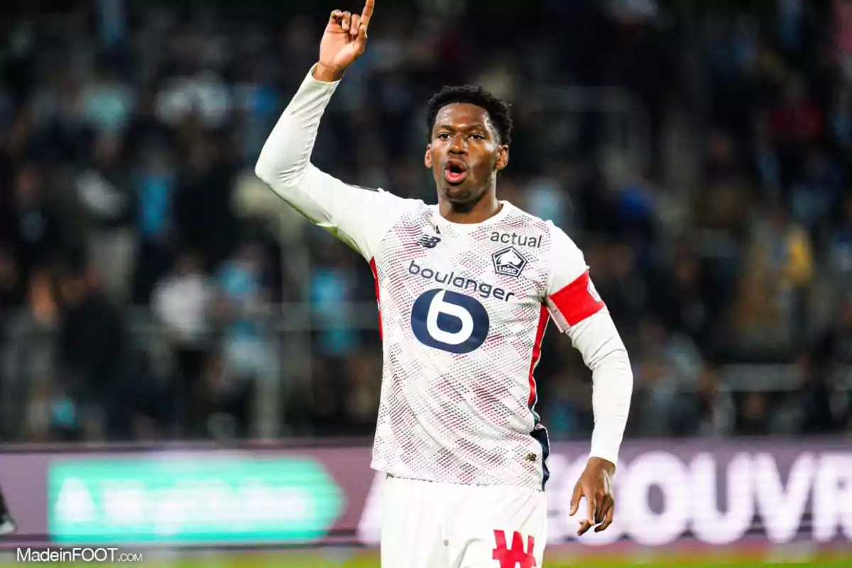 Jugador de fútbol con uniforme blanco y rojo levantando un brazo en un estadio.