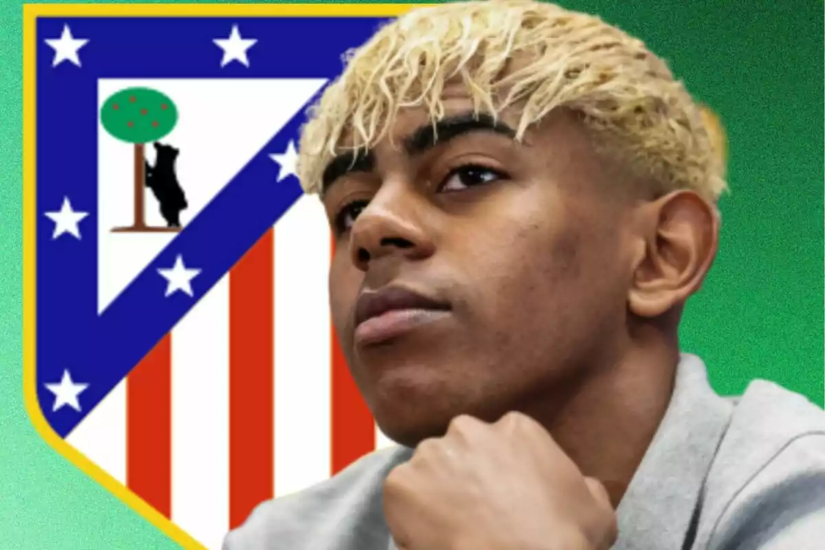 Un joven con cabello rubio claro posa frente al escudo del Atlético de Madrid sobre un fondo verde.