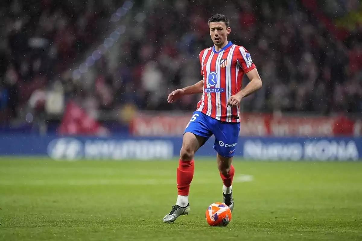 Futbolista del Atlético de Madrid con uniforme rojo y blanco controlando el balón en un partido bajo la lluvia Futbolista del Atlético de Madrid con uniforme rojo y blanco controlando el balón en un partido bajo la lluvia