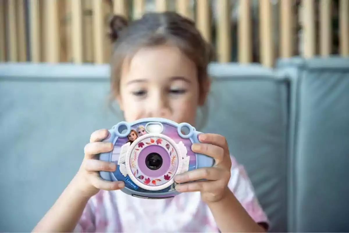 Una niña sostiene una cámara de juguete decorada con personajes de una película animada. Una niña sostiene una cámara de juguete decorada con personajes de una película animada.