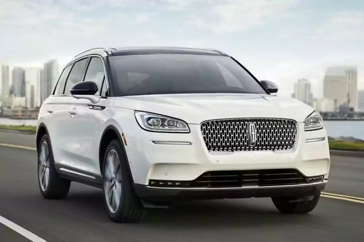 Camioneta SUV blanca circulando por una carretera con edificios al fondo Camioneta SUV blanca circulando por una carretera con edificios al fondo