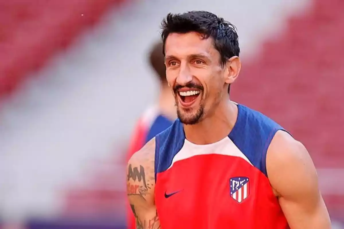 Un jugador de fútbol sonríe durante un entrenamiento, vistiendo una camiseta sin mangas del Atlético de Madrid.