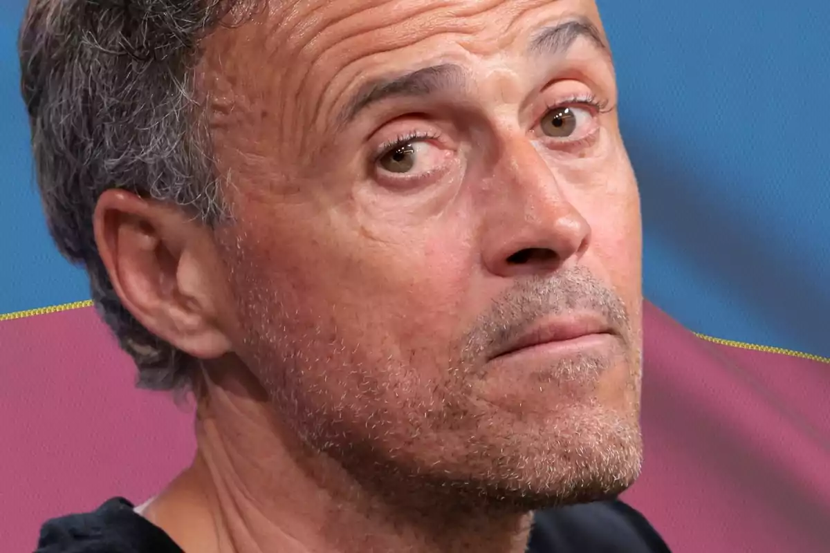 Luis Enrique mirando a cámara de costado sobre un fondo azul y rojo