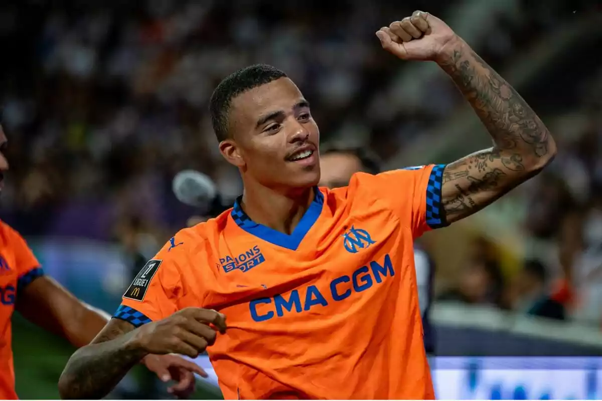 Soccer player celebrating with his fist raised while wearing an orange CMA CGM team uniform.