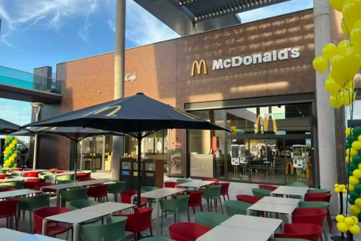 Entrada de un restaurante de comida rápida con mesas y sillas al aire libre y decoración con globos amarillos y verdes. Entrada de un restaurante de comida rápida con mesas y sillas al aire libre y decoración con globos amarillos y verdes.
