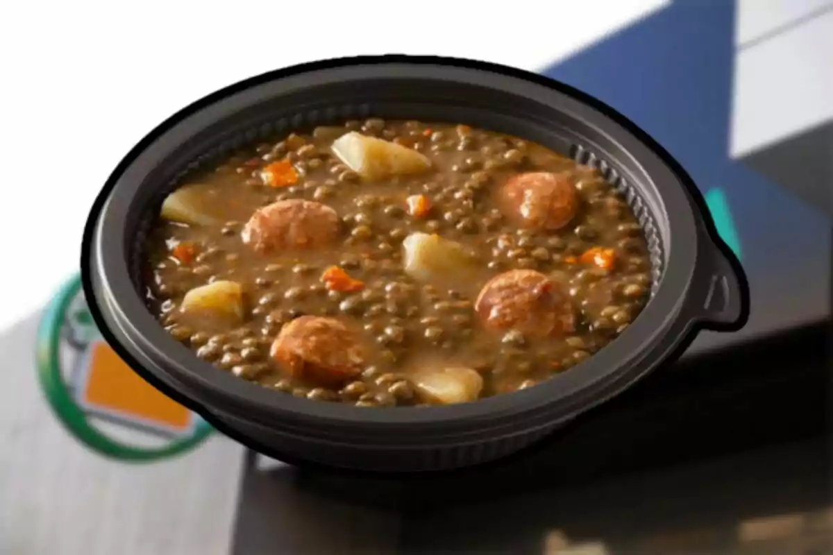 A plate of lentils with chorizo and potatoes in a black container. A plate of lentils with chorizo and potatoes in a black container.