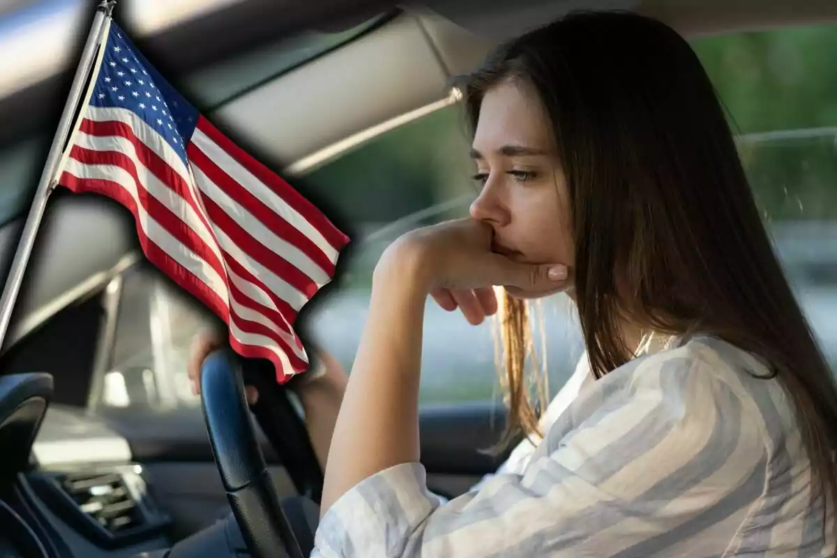 Mujer pensativa sentada al volante de un auto con una bandera de Estados Unidos al frente.