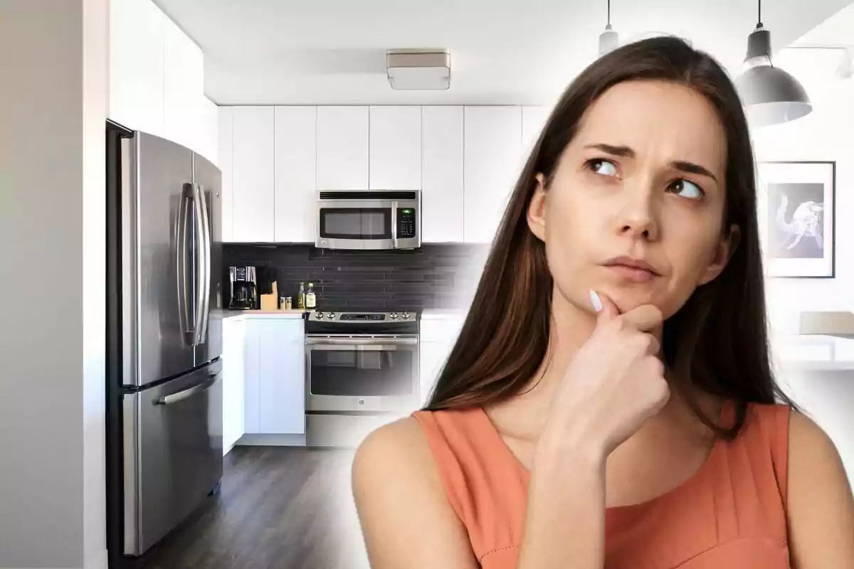 Una mujer pensativa en una cocina moderna con electrodomésticos de acero inoxidable.