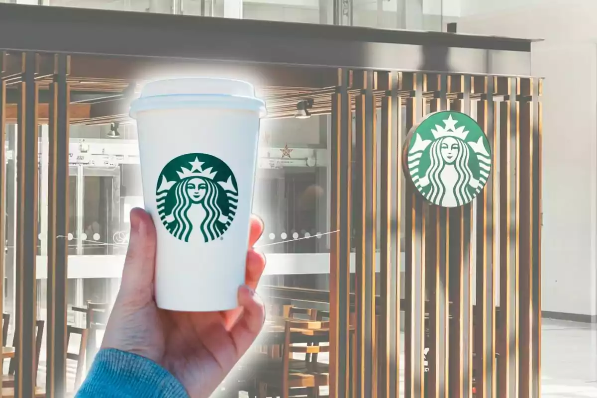 Una mano sostiene un vaso de café frente a un establecimiento con el logotipo de una sirena verde, el cual es Starbucks.
