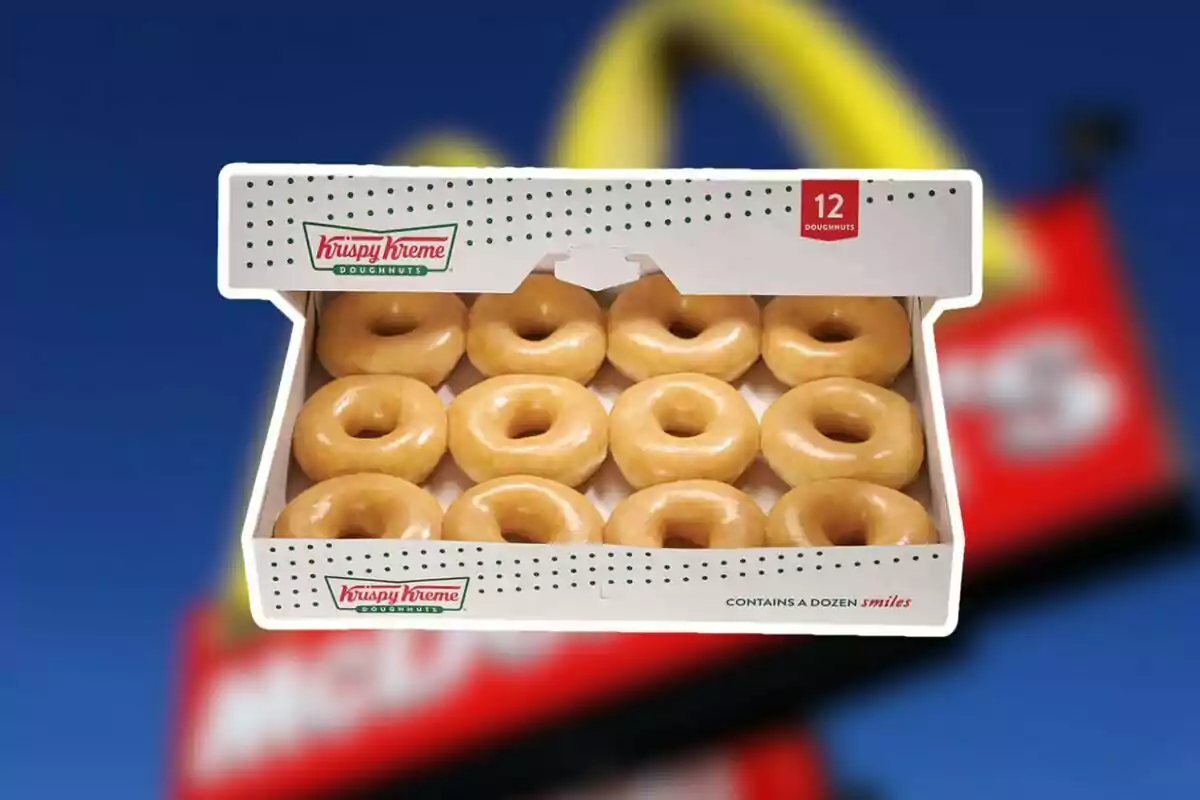 Una caja de donas glaseadas de Krispy Kreme con doce unidades frente a un fondo borroso de un letrero de McDonald's. Una caja de donas glaseadas de Krispy Kreme con doce unidades frente a un fondo borroso de un letrero de McDonald's.