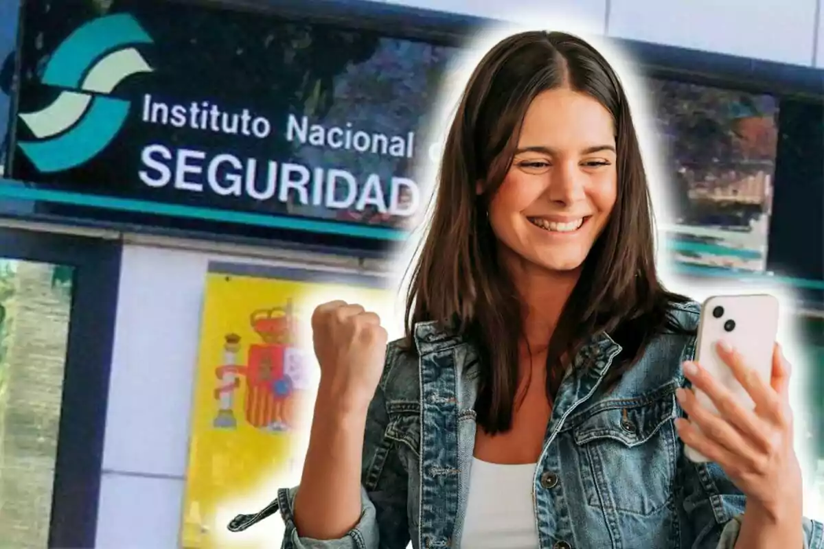 Una mujer sonriente con una chaqueta de mezclilla sostiene un teléfono móvil mientras celebra con el puño levantado frente a un edificio del Instituto Nacional de Seguridad.