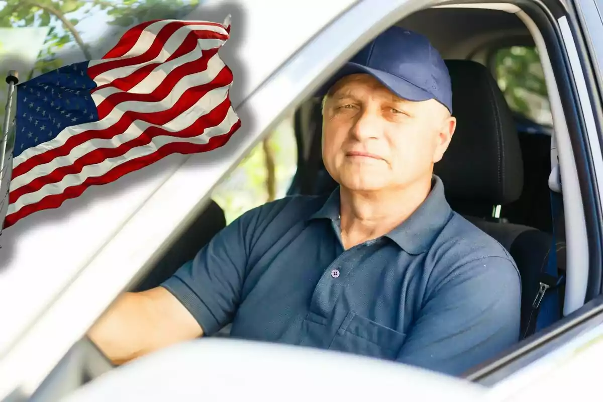 Hombre mayor con gorra azul sentado al volante de un auto y una bandera de Estados Unidos ondeando al fondo
