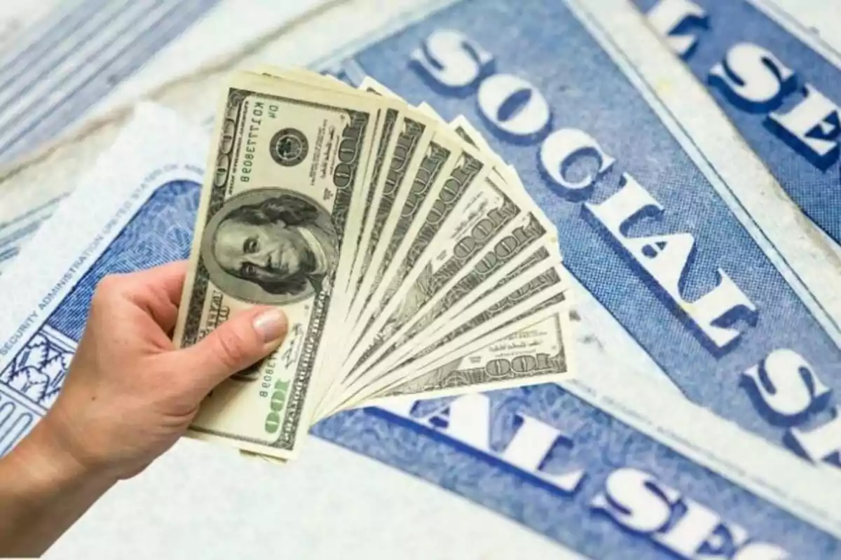 Hand holding several hundred-dollar bills over United States Social Security cards