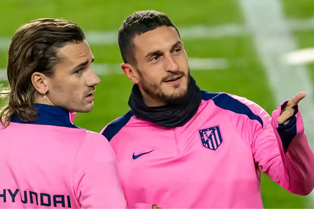 Dos jugadores del Atlético de Madrid conversando en el campo con uniformes de entrenamiento rosa.