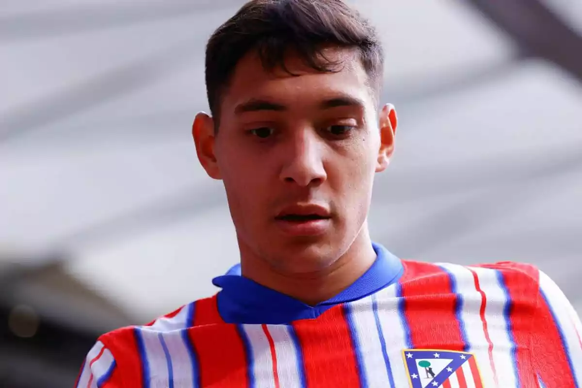 Un jugador de fútbol con la camiseta del Atlético de Madrid mirando hacia abajo.