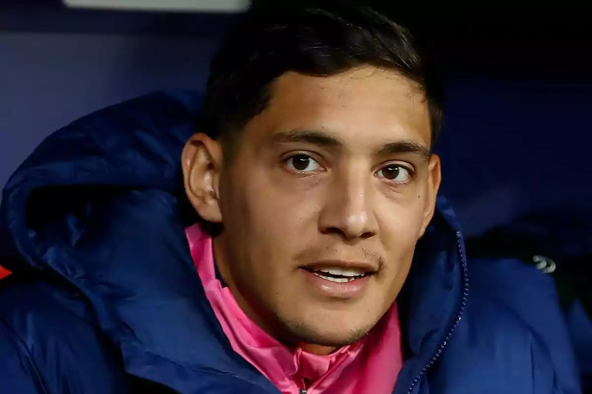 A man in a blue jacket and pink T-jersey looks into the camera.