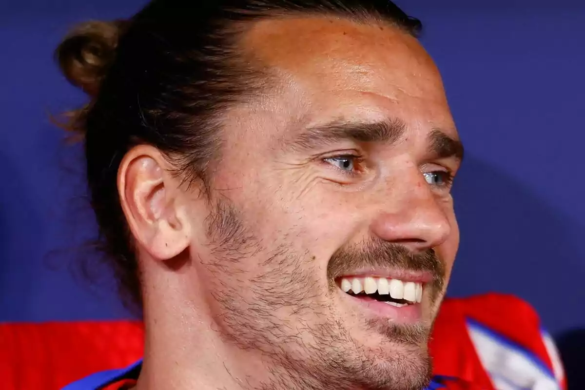 Un hombre sonriente con barba y cabello recogido, mirando hacia la derecha.