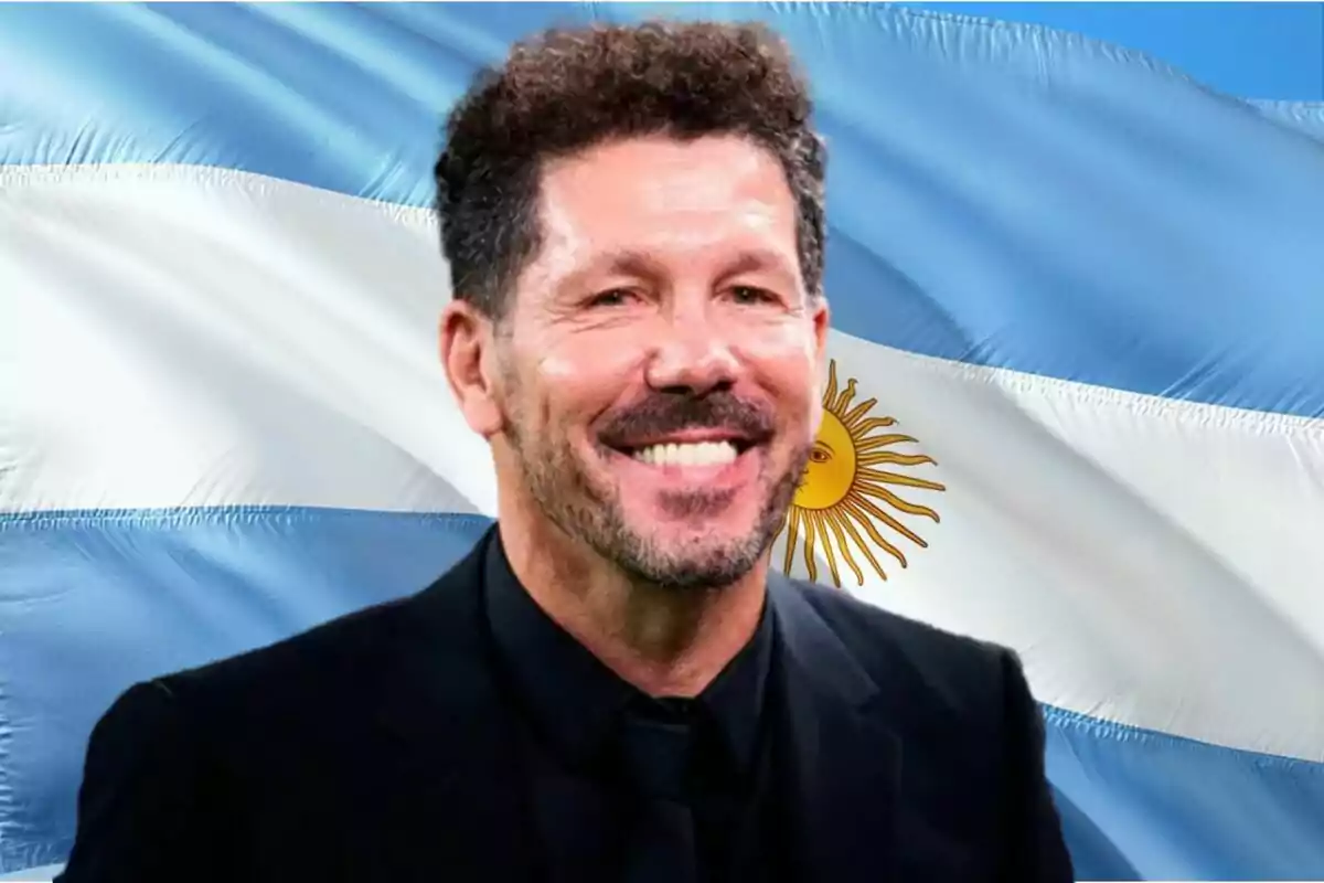 A smiling man in a dark suit in front of a waving Argentine flag.