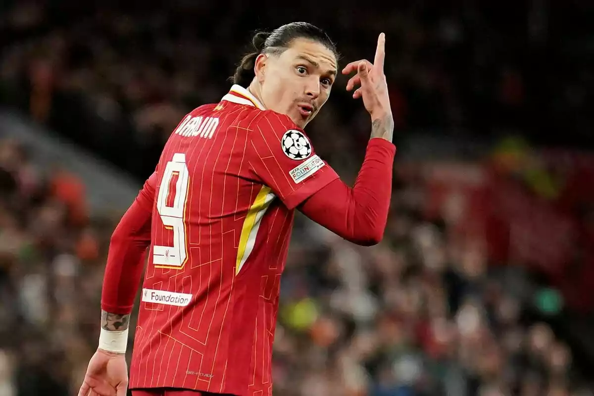 Jugador de fútbol con camiseta roja y número 9 en la espalda gesticulando con la mano durante un partido.