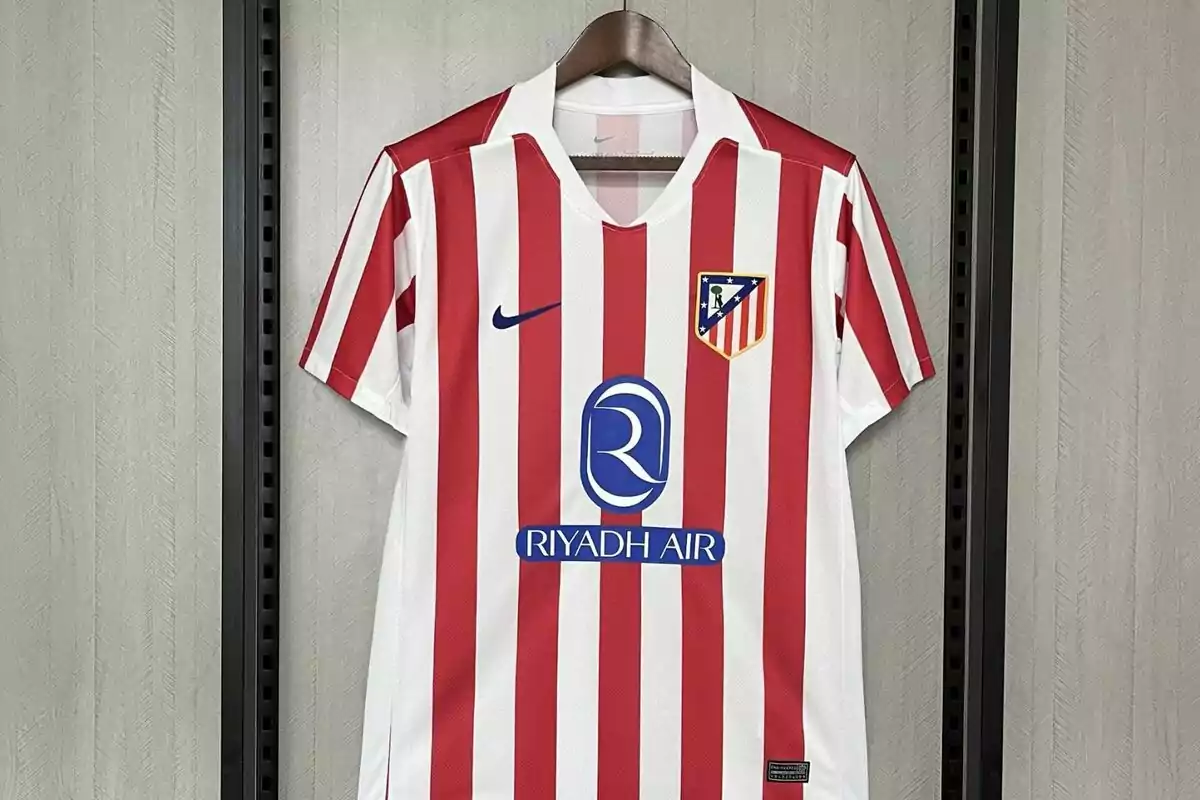 Camiseta de fútbol con rayas verticales rojas y blancas, logo de Nike y escudo de un equipo en el pecho, colgada en un perchero. Camiseta de fútbol con rayas verticales rojas y blancas, logo de Nike y escudo de un equipo en el pecho, colgada en un perchero.