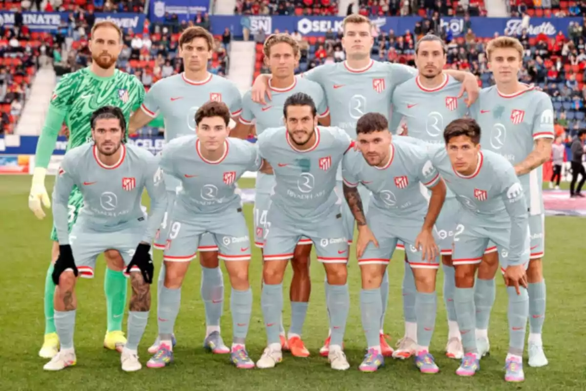 Un equipo de fútbol posando en el campo antes de un partido, todos con uniformes grises y un portero con uniforme verde. Un equipo de fútbol posando en el campo antes de un partido, todos con uniformes grises y un portero con uniforme verde.