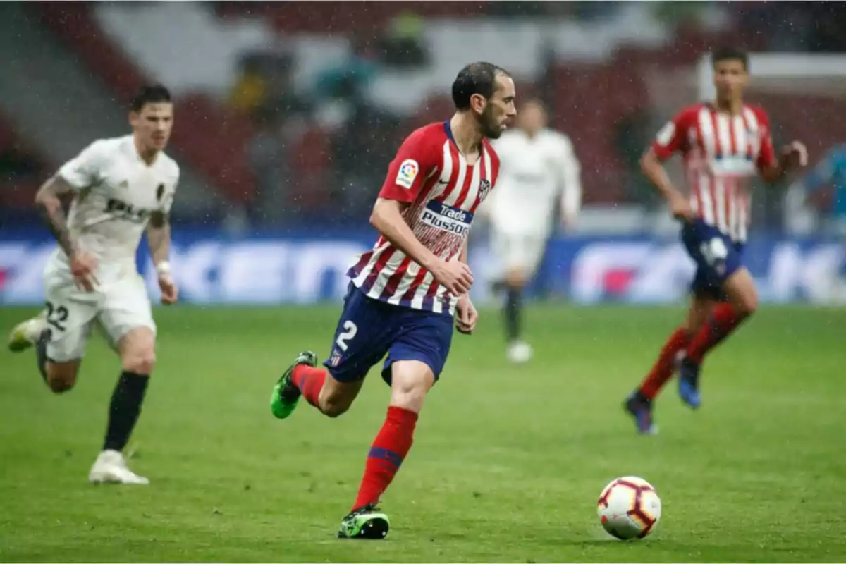 Un jugador de fútbol con uniforme a rayas rojas y blancas corre con el balón en un campo de juego mientras otros jugadores lo siguen. Un jugador de fútbol con uniforme a rayas rojas y blancas corre con el balón en un campo de juego mientras otros jugadores lo siguen.