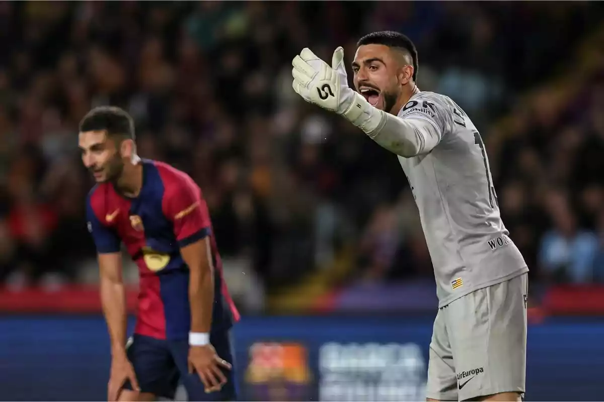 Portero vestido de gris gritando y gesticulando con el brazo extendido mientras un jugador con uniforme azul y rojo se inclina hacia adelante en el campo de fútbol Portero vestido de gris gritando y gesticulando con el brazo extendido mientras un jugador con uniforme azul y rojo se inclina hacia adelante en el campo de fútbol