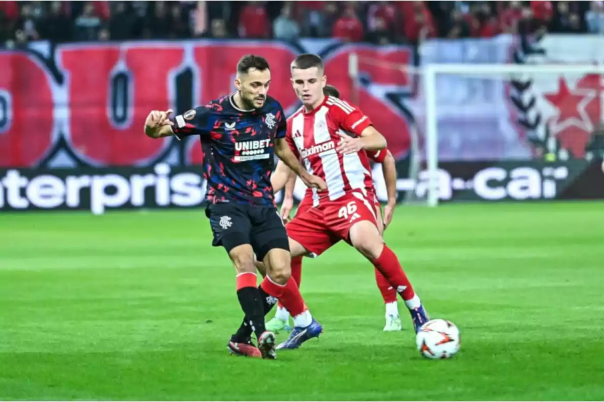 Dos futbolistas disputan el balón durante un partido en un estadio lleno de aficionados Dos futbolistas disputan el balón durante un partido en un estadio lleno de aficionados