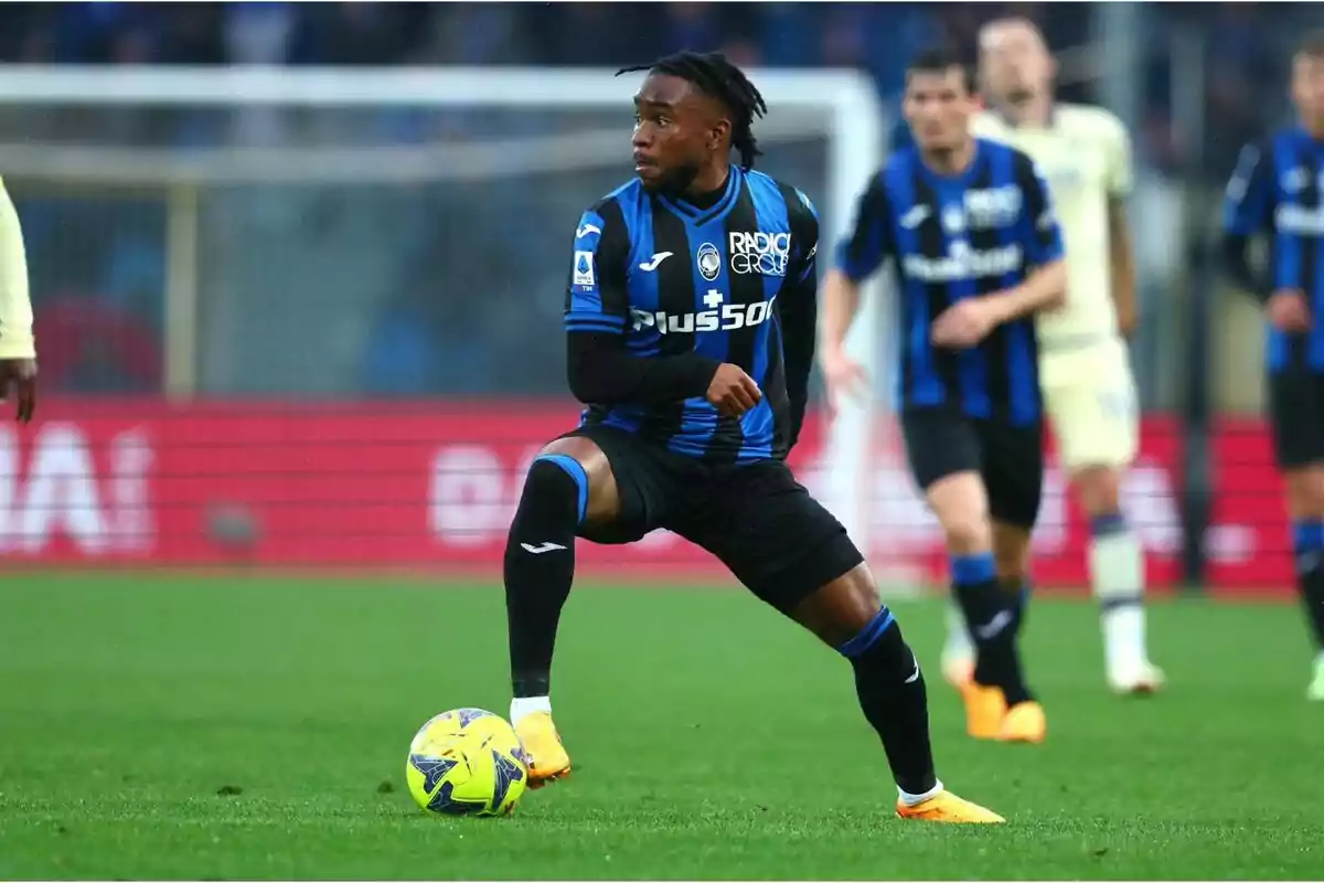 Jugador de fútbol con uniforme azul y negro controlando el balón en el campo durante un partido.