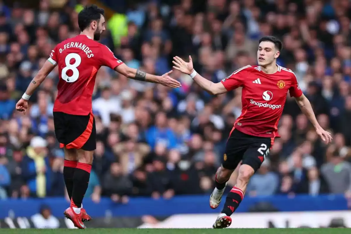 Dos jugadores de fútbol con uniforme rojo se dan la mano en el campo durante un partido.