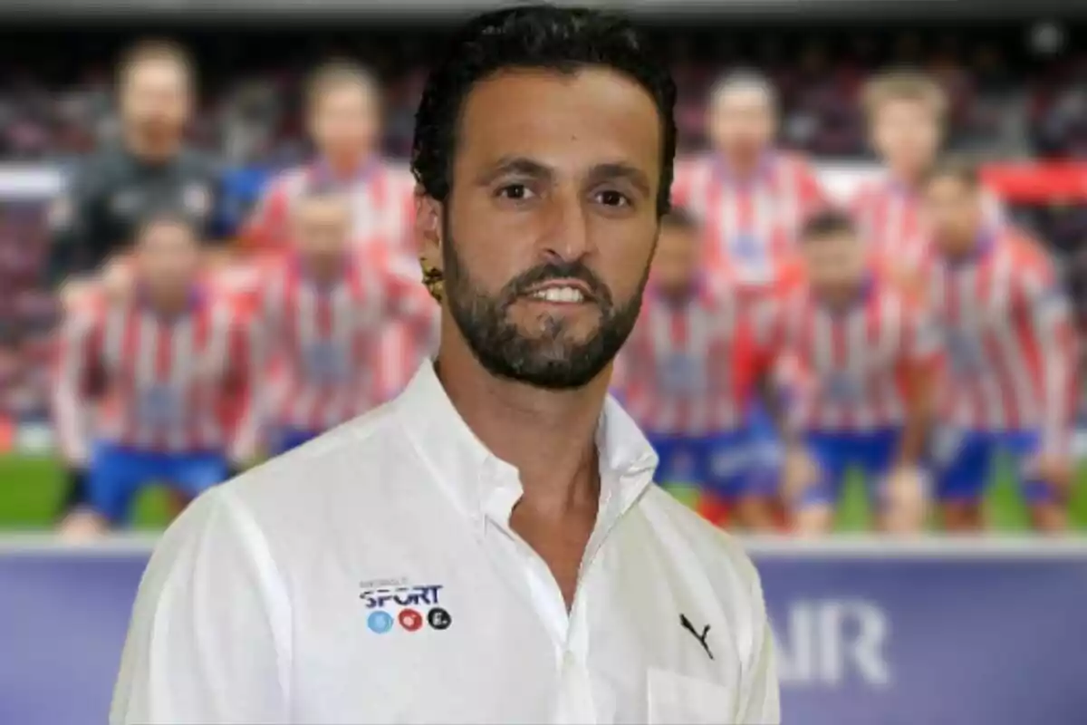 Un hombre con barba y camisa blanca está de pie frente a un fondo borroso de un equipo de fútbol con uniformes a rayas rojas y blancas.