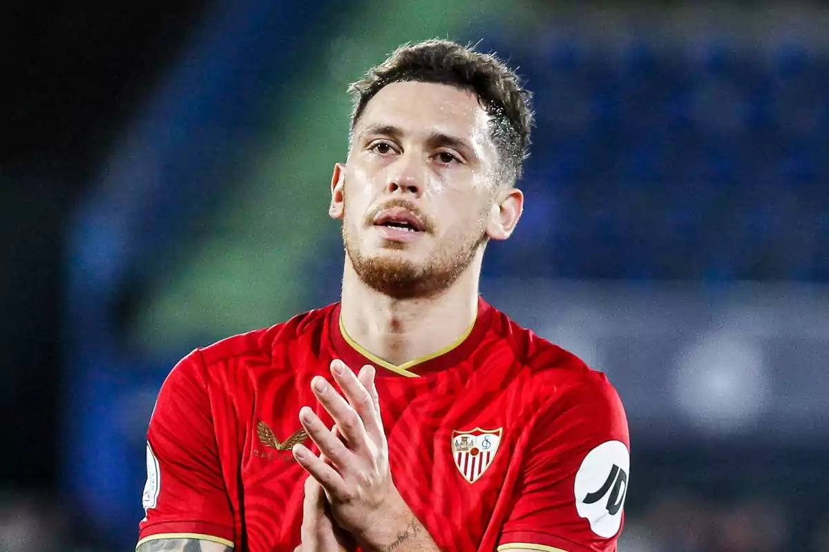 Un jugador de fútbol con la camiseta roja del Sevilla FC aplaudiendo en el campo.