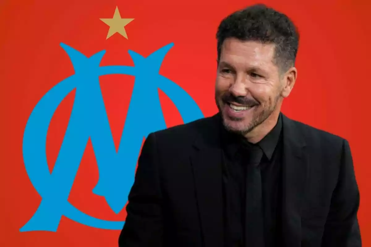 Un hombre sonriente con traje negro frente a un fondo rojo con un logotipo azul y una estrella dorada.