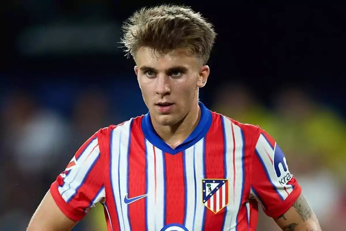 Jugador de fútbol con camiseta a rayas rojas y blancas del Atlético de Madrid en el campo.