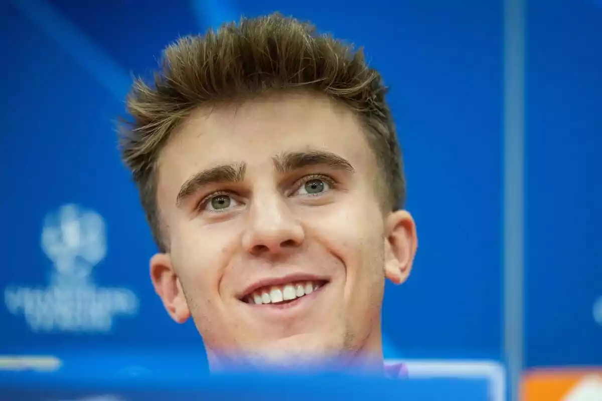 A young man smiling in front of a blue background.