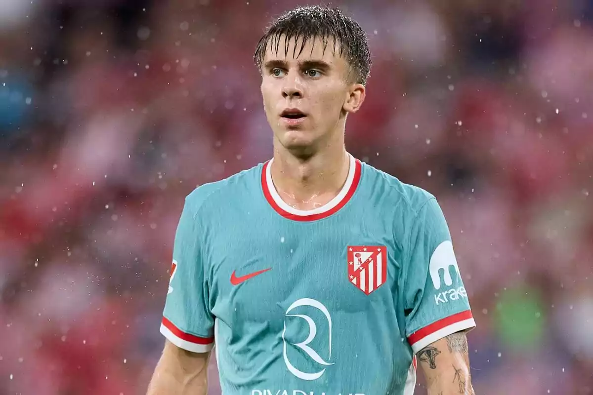 Jugador de fútbol con camiseta del Atlético de Madrid en un partido bajo la lluvia.