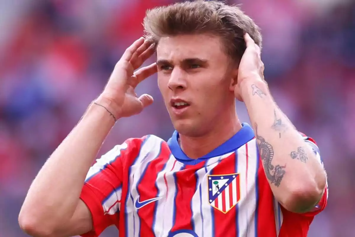 Jugador de fútbol con camiseta del Atlético de Madrid se lleva las manos a la cabeza durante un partido.