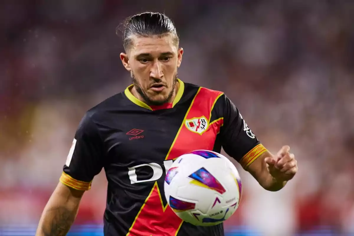 Jugador de fútbol con uniforme negro y rojo controlando un balón en un partido.