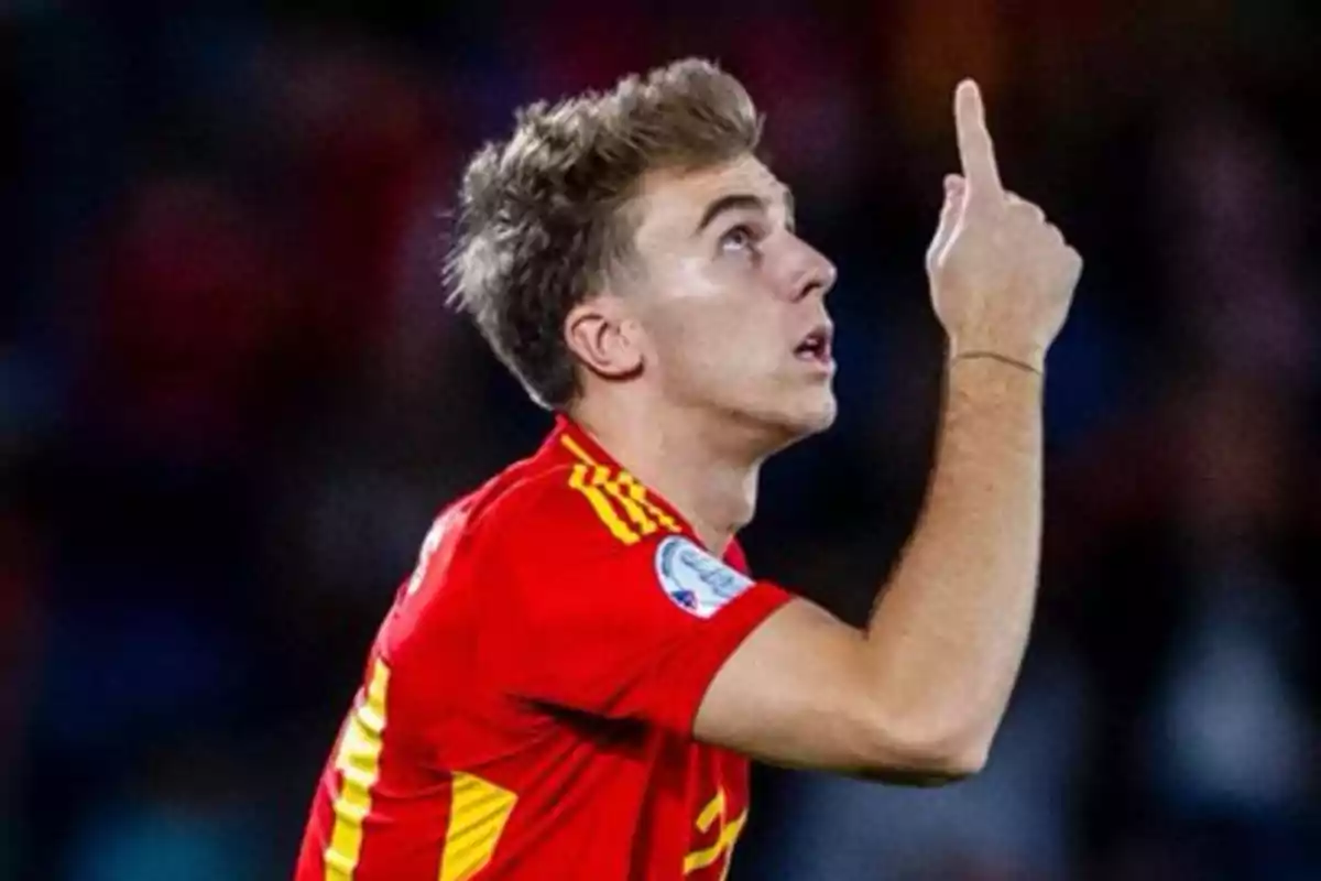 Un jugador de fútbol con uniforme rojo señala hacia arriba durante un partido.