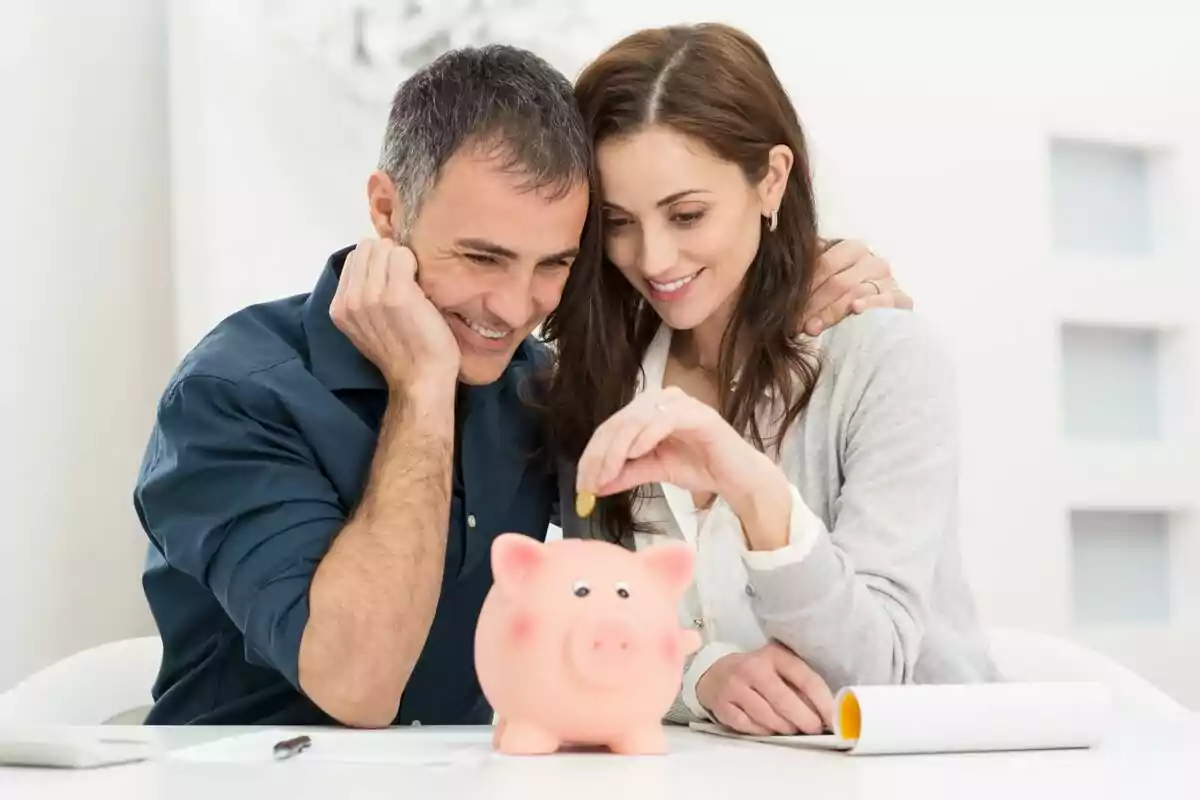 Una pareja sonriente colocando una moneda en una alcancía de cerdito. Una pareja sonriente colocando una moneda en una alcancía de cerdito.